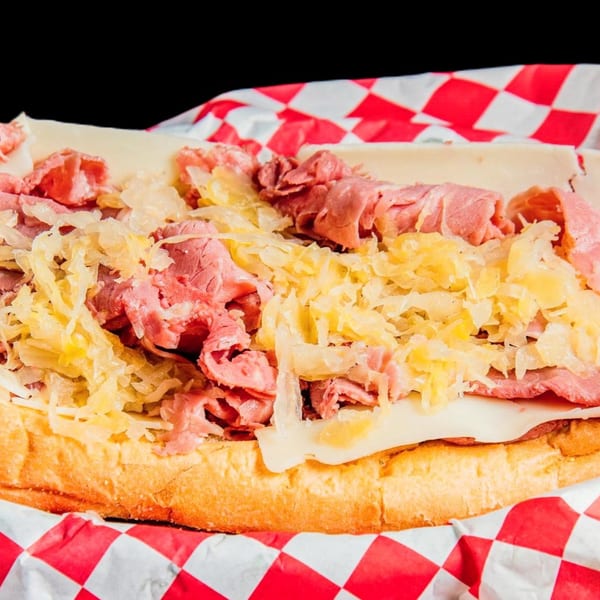 A close-up of a loaded Reuben sandwich with pastrami, Swiss cheese, and sauerkraut on a bun.