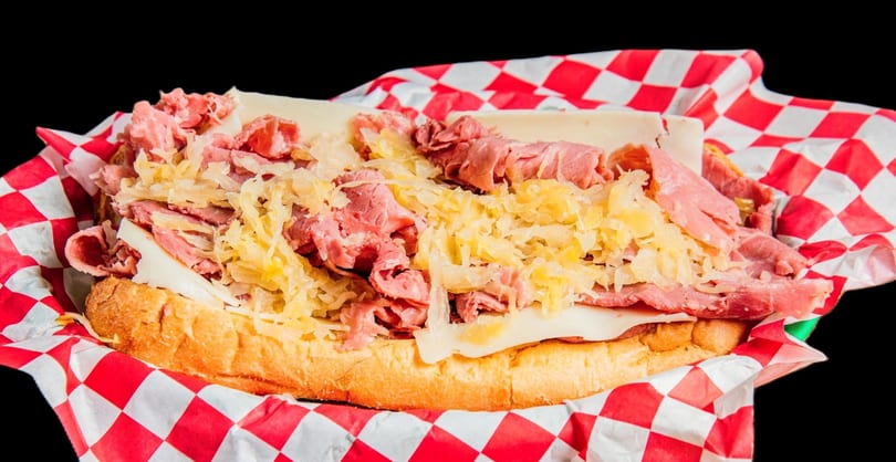 A close-up of a loaded Reuben sandwich with pastrami, Swiss cheese, and sauerkraut on a bun.